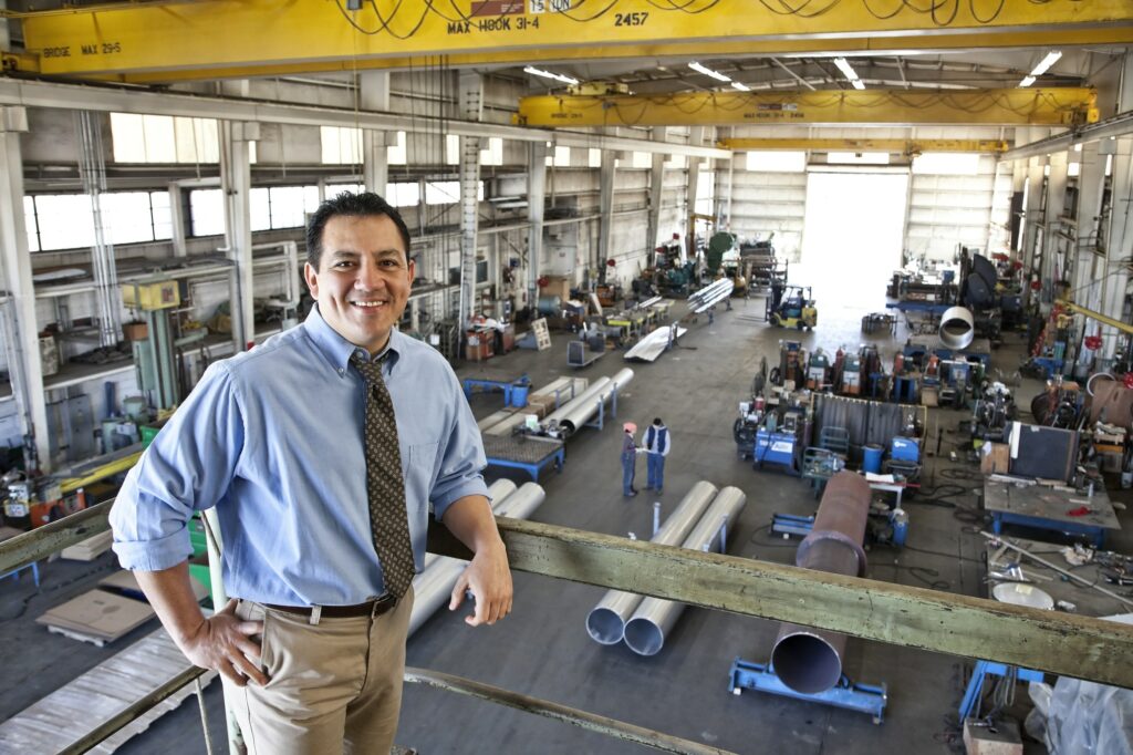 hispanic man owner of a sheet metal factory stanidng above factory floor